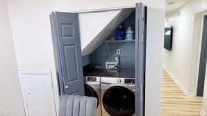 A compact laundry room with a washing machine, dryer, and storage shelves. - Your Home: Three bedrooms, accommodating 6 guests. (Columbus)