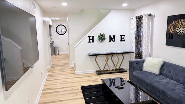 A modern living room with a sofa, a coffee table, a TV, a staircase, and a 'HOME' sign on the wall. - Your Home: Three bedrooms, accommodating 6 guests. (Columbus)