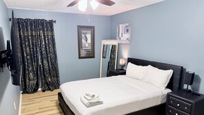 A bedroom with a bed, a nightstand, a lamp, a ceiling fan, and a patterned rug. - Your Home: Three bedrooms, accommodating 6 guests. (Columbus)