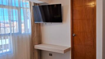 A hotel room with a bed, a mounted TV, a wooden door, and a window with curtains.