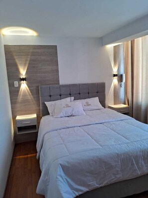 A modern bedroom with a large bed, two bedside tables with integrated lighting, a wooden accent wall, and a neutral color scheme. - Hotel EL Virrey Suite (Espinar)