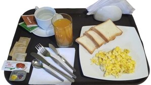 En bakke med morgenmad, inklusive røræg, ristet brød, et glas appelsinjuice, en kop kaffe og tilbehør.