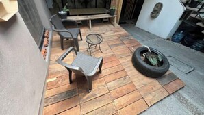Un patio con piso de madera, dos sillas grises, una mesa redonda pequeña y un columpio hecho con neumático.