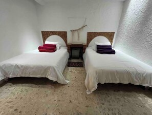 Two single beds with wooden headboards and white bedding, a small table and chair, and a hanging light fixture.