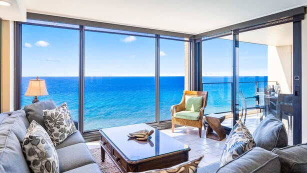 A balcony with a view of the ocean, furnished with a sofa, armchair, and table.
