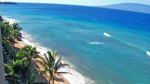 A beach with clear blue water, palm trees, and a distant mountain. - Beachfront on Kaanapali Mahana 1106! (Lahaina)