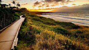 Une promenade en bois menant à une plage offrant une vue sur l’océan, des palmiers et un coucher de soleil.