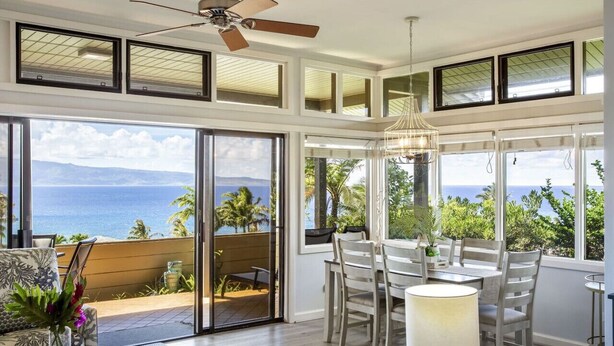 Une pièce spacieuse dotée d’une grande porte-fenêtre coulissante donnant sur un balcon avec vue sur l’océan. On y trouve un coin repas avec une table et des chaises, ainsi qu’un ventilateur de plafond.