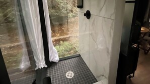 Een moderne badkamer met een douchecabine van glas, een witte wastafel en een marmeren wand.