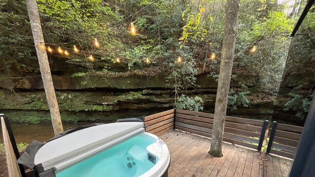 Een hottub op een houten terras met een rotsachtige achtergrond en lichtjes.