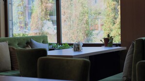 A modern room with a green sofa, a small table, and a window with a view of trees and buildings. - Hotel Citadela (Sarajevo)