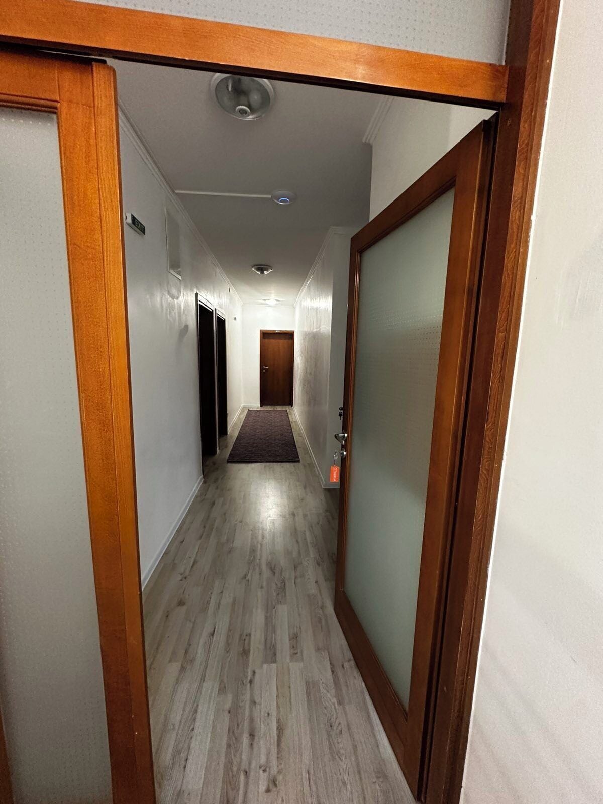 Un couloir avec des boiseries, un sol recouvert de moquette et une porte dotée d’un panneau en verre dépoli.