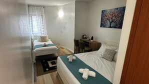 A compact hotel room with two single beds, a small table, a chair, a painting on the wall, and a wooden floor. - Hotel Citadela (Sarajevo)