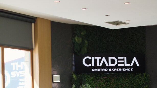 A restaurant interior with green upholstered chairs, a wooden table, and a wall with a green leafy design. - Hotel Citadela (Sarajevo)