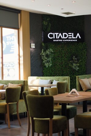 A restaurant interior with green upholstered chairs, a wooden table, and a wall with a green leafy design. - Hotel Citadela (Sarajevo)