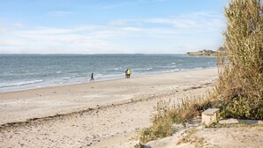 Una spiaggia con una battigia sabbiosa, alcune persone che passeggiano e un edificio in lontananza.