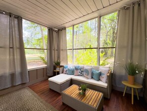 Ein gemütliches Zimmer mit großem Fenster, einer gepolsterten Bank, einem kleinen Tisch und einem Blumentopf.