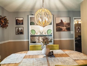 A dining area with a round table, a chandelier, and wall-mounted shelves with decorative items.
