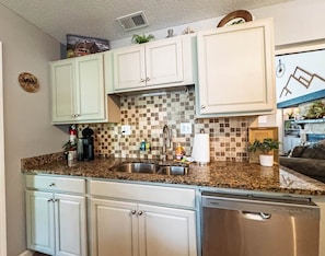 A kitchen with white cabinets, a granite countertop, a stainless steel sink, and a dishwasher.