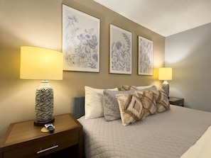 A hotel room with a bed, two bedside lamps, a decorative vase, and three framed botanical prints on the wall.