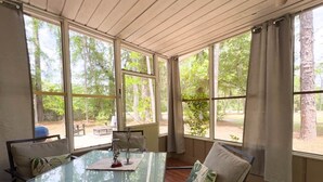 Un invernadero con una mesa y sillas de vidrio, ventanas amplias y vistas a árboles.