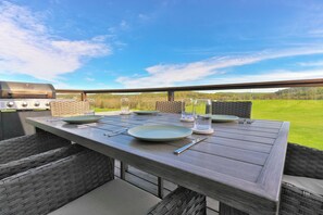 Ein Essbereich im Freien mit Grill, Korbmöbeln und Blick auf eine Wiese.