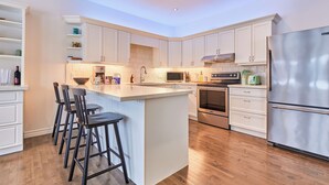 A modern kitchen with white cabinets, a stainless steel refrigerator, a microwave, an oven, and a large island with bar stools.
