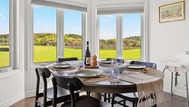 A dining room with a table set for four, large windows, and a view of a green landscape.
