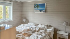 Et soveværelse med en seng, sengeborde, lamper, et vindue og et billede i ramme på væggen.