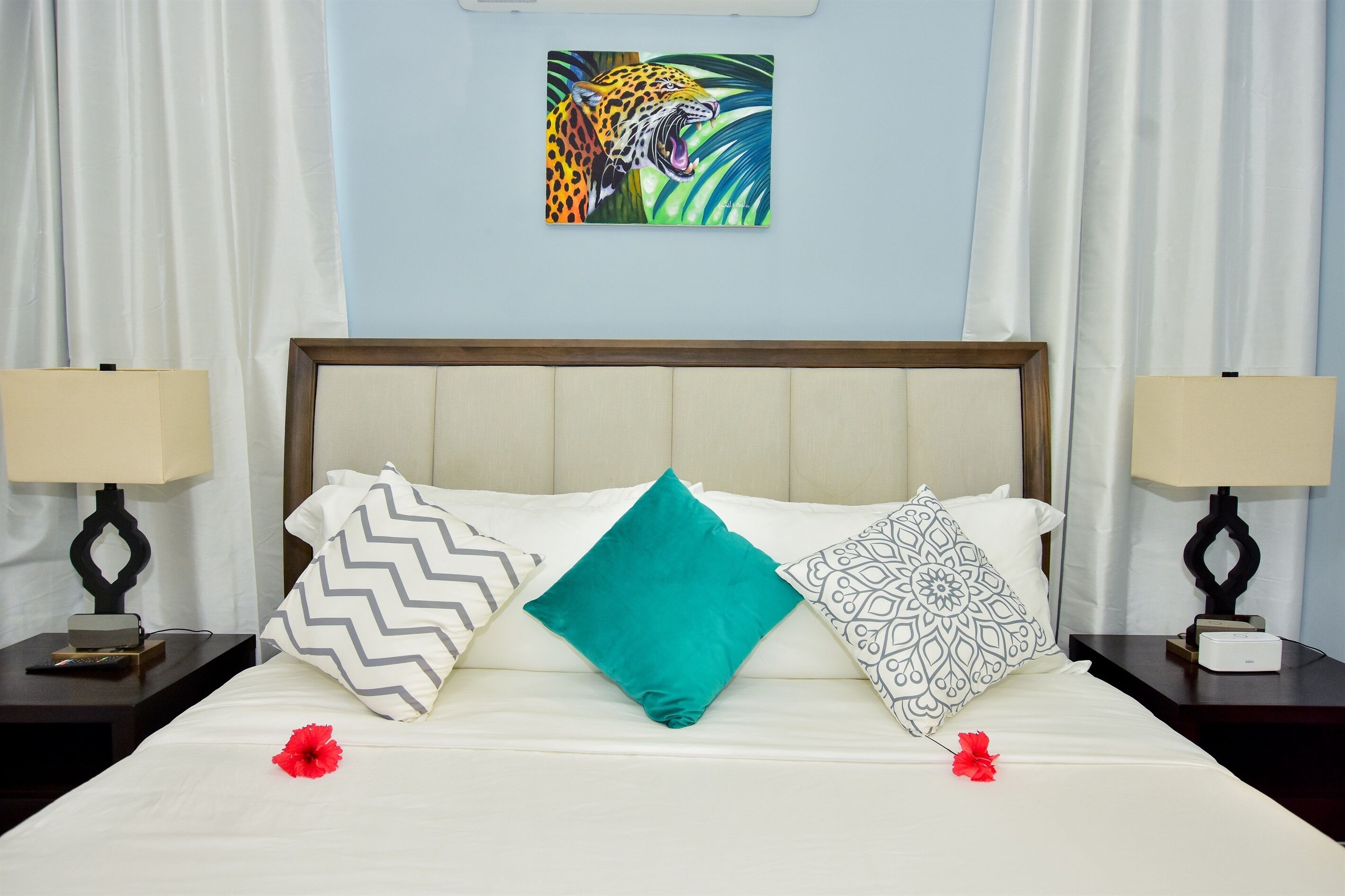 A hotel room with a bed, two nightstands, a painting of a jaguar, and decorative pillows.