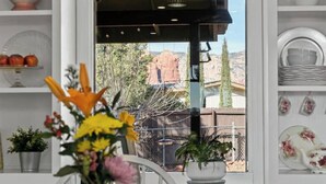 A room with a view of a red rock formation, a white chair, and a table with a vase of flowers. - The Tourist & Hiking Spot!

 (Sedona)