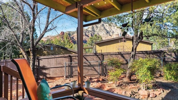 A patio with a wooden bench, a covered area, and a view of a fenced yard with trees and a building in the background. - The Tourist & Hiking Spot!

 (Sedona)