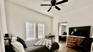 Ein Schlafzimmer mit einem Bett, einem Schreibtisch, einem Stuhl, einem Fernseher und einem Deckenventilator.