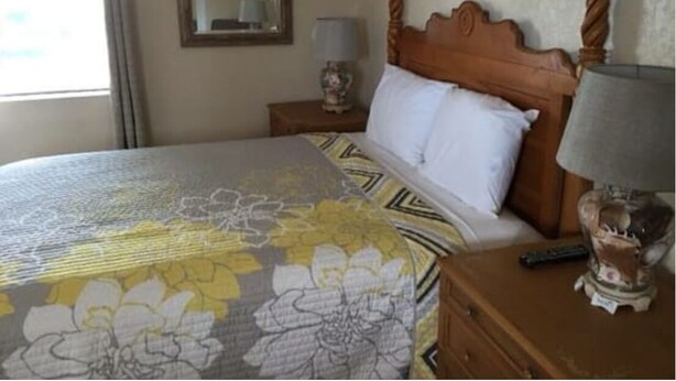 A hotel room with a bed, a nightstand, a lamp, and a mirror.