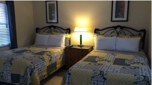 A room with two beds, each with a patterned bedspread, a nightstand with a lamp, and a framed picture on the wall.
