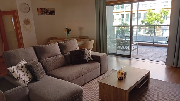 A modern living room with a sectional sofa, a coffee table, and a view of a balcony with outdoor furniture.
