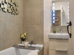 A bathroom with a bathtub, a sink, a mirror, and a wall-mounted light fixture.