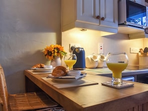 Une table en bois dressée pour le petit-déjeuner, avec des croissants, une machine à café et un verre de jus d’orange.