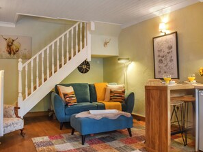 A living room with a staircase, a sofa, a coffee table, a lamp, and a dining area with chairs and a table.
