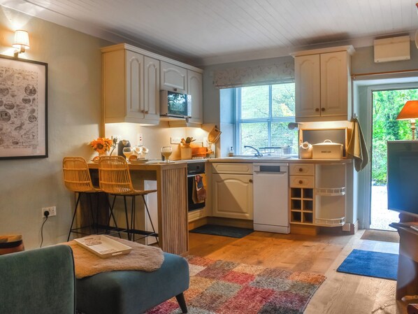 A compact kitchen with white cabinetry, a dining area with wicker chairs, and a view of greenery outside.