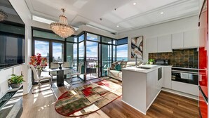 A modern kitchen with large windows, a central island, and a dining area with a view. - Penthouse Crown Jewel (Auckland)