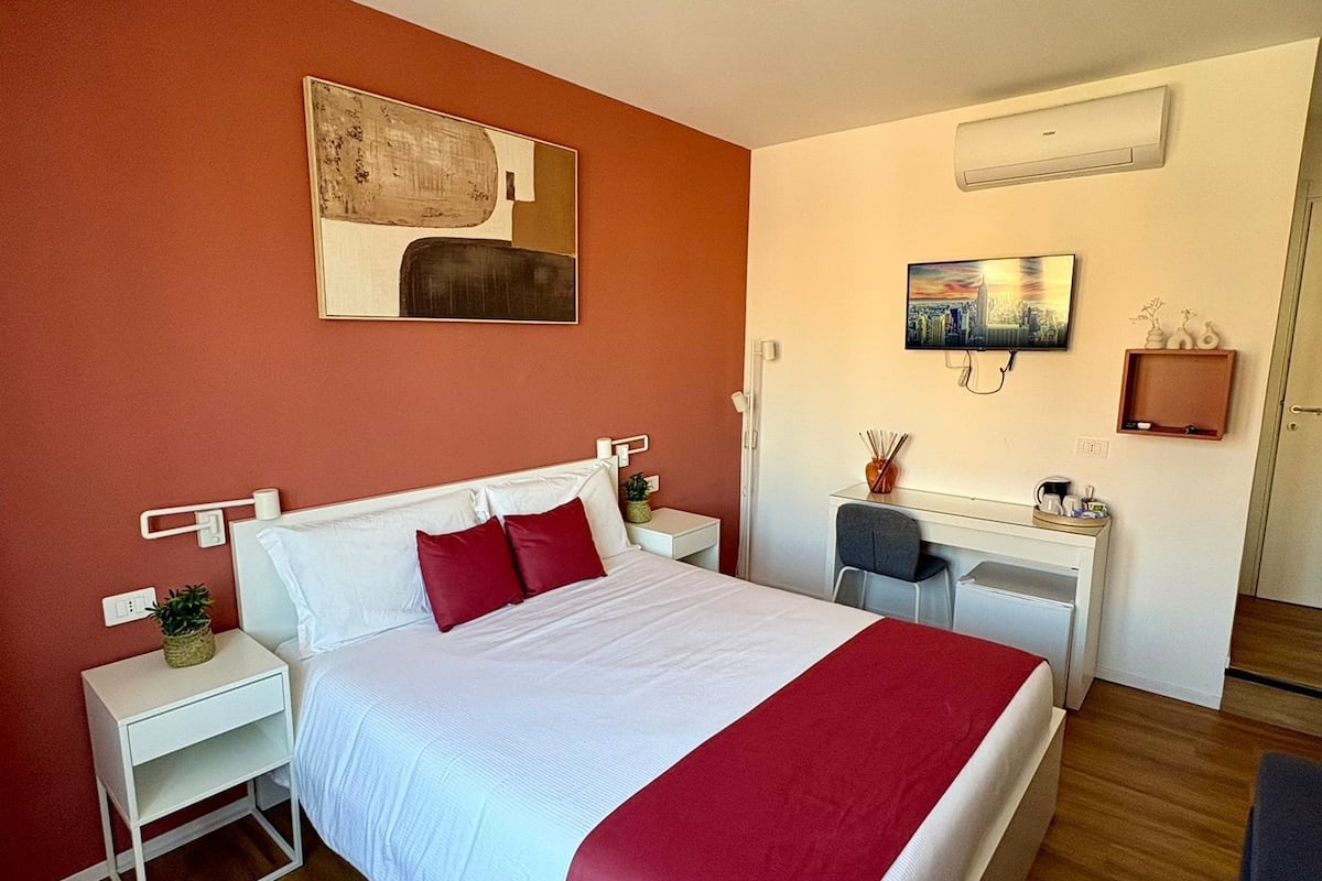 Habitación de hotel con cama, mesita de noche, escritorio, silla y obras de arte en las paredes.
