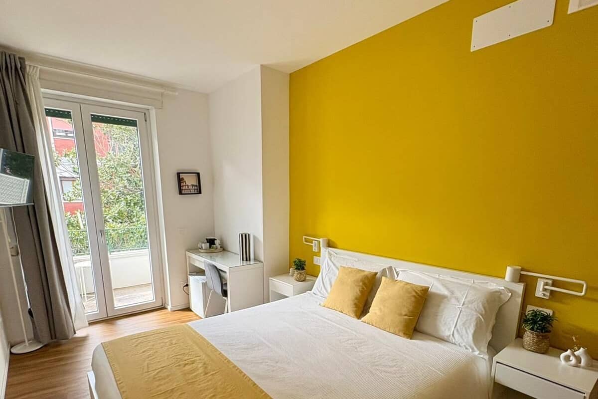 Un dormitorio con una cama, mesitas de noche, un escritorio, una silla y una ventana con cortinas.