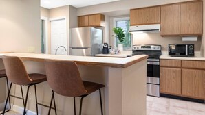 Une cuisine moderne dotée d’un îlot central, de deux tabourets de bar, d’appareils électroménagers en acier inoxydable et de meubles de rangement en bois.