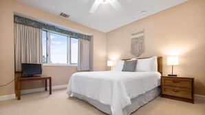 Une chambre d’hôtel avec un grand lit, une table de chevet avec une lampe, un téléviseur posé sur un meuble et une fenêtre avec des rideaux.