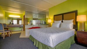 Una habitación de hotel con cama, escritorio, silla, espejo y una bañera roja.