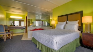 Quarto de hotel com cama, escrivaninha, cadeira, espelho e uma banheira vermelha.