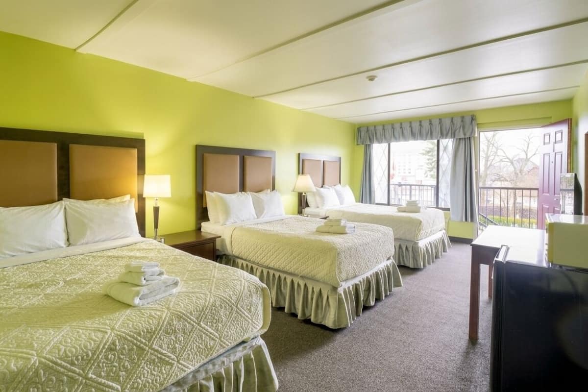 A hotel room with three beds, a desk, and a chair.