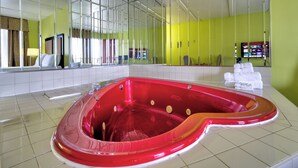 Un jacuzzi rojo en una habitación de hotel con un espejo grande y una pared verde.