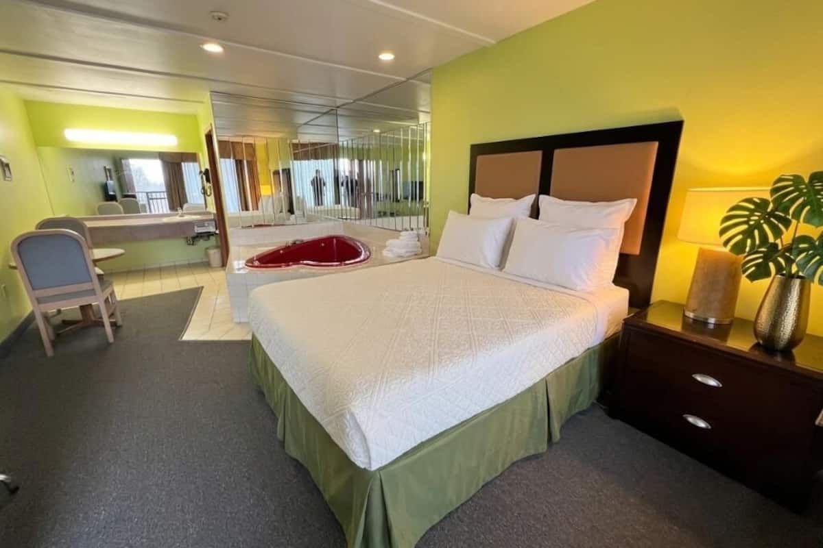 A hotel room with a large bed, a bedside table with a lamp, a chair, and a mirror.